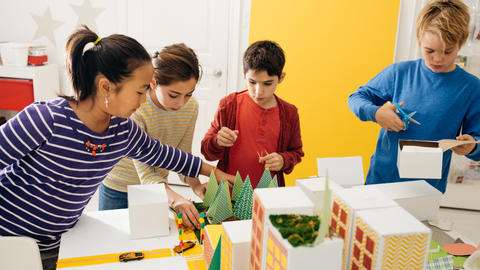 children collaborating on a hands-on classroom project, building a model city with paper buildings and trees