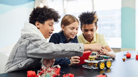 Three students collaborate on building and programming a small wheeled robot during a hands-on STEM project