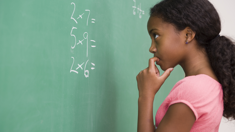 Young student thoughtfully solving multiplication problems on a board during class