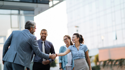 Professionals smiling and shaking hands outside a modern office building, symbolizing school-industry collaboration